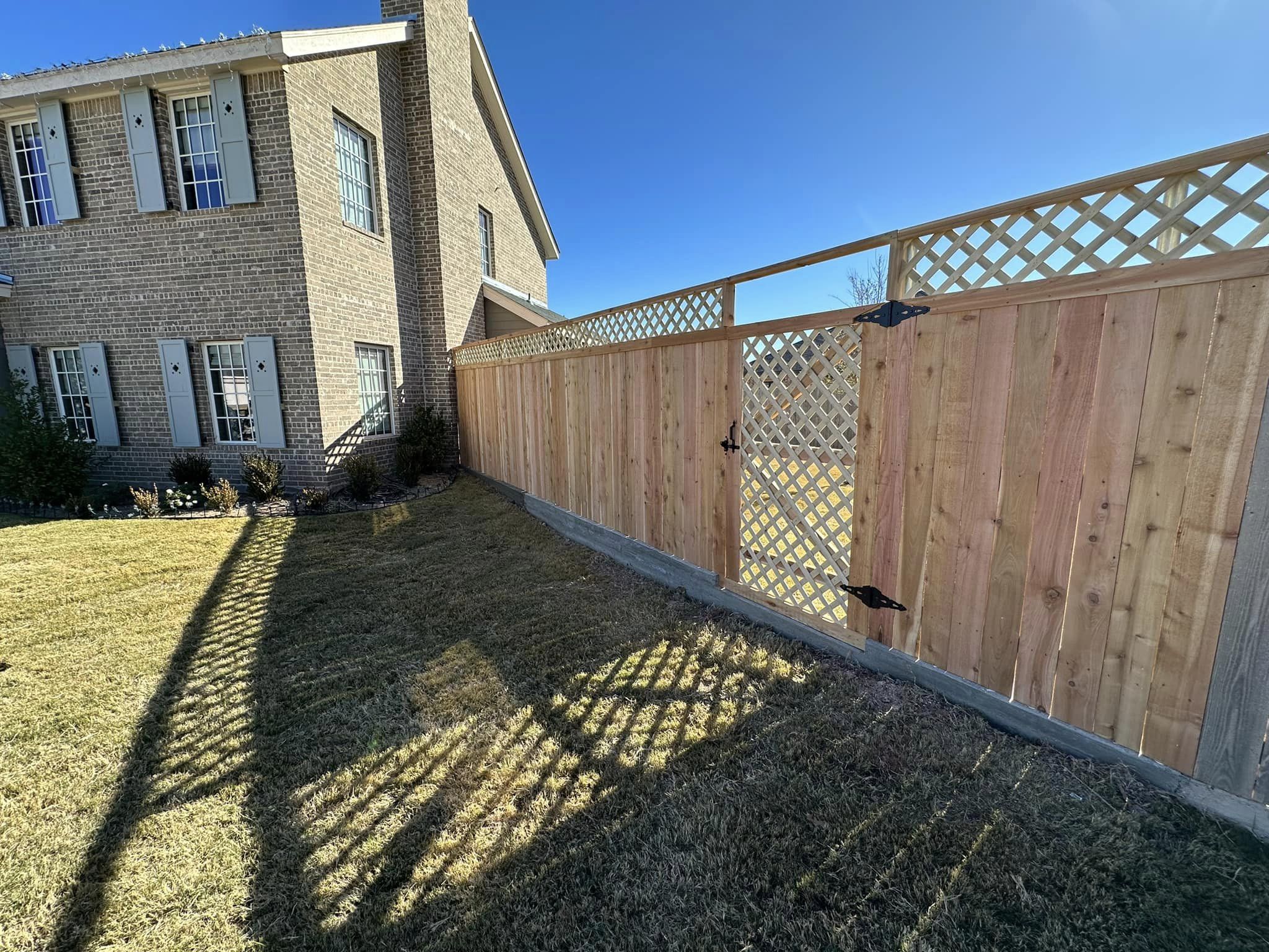 Fortress wood privacy fence and lattice gate beside a brick home